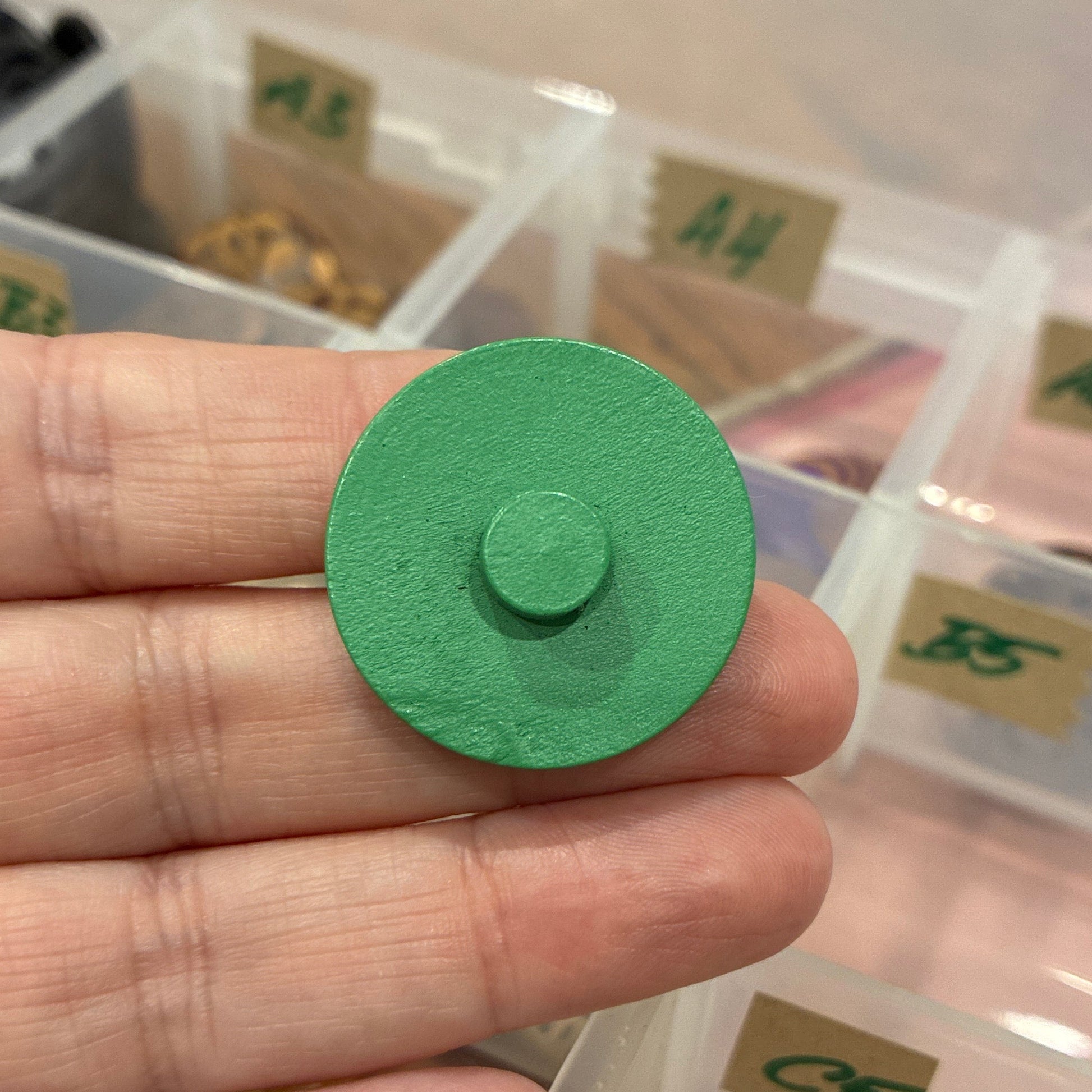 Green button held in front of a container with various buttons.