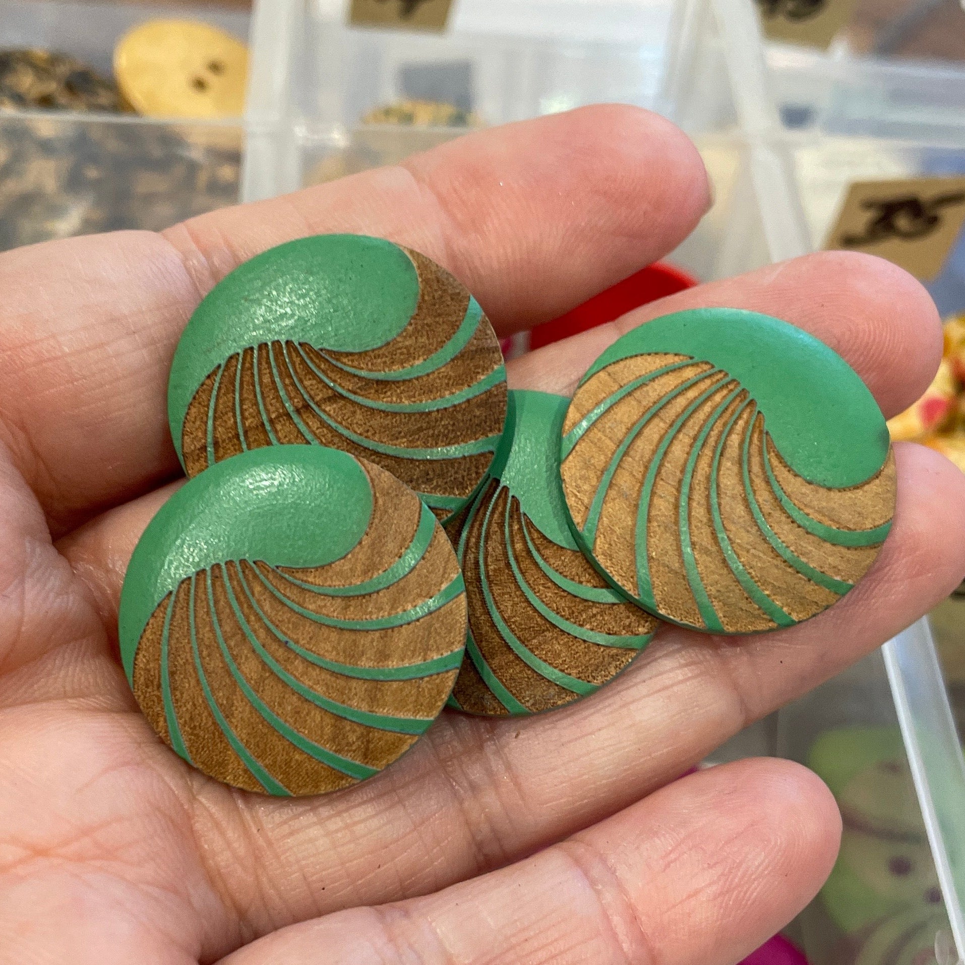 Hand holding green buttons with a background of a button collection organizer.