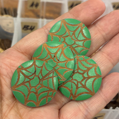 Hand holding green buttons with brown patterns against a blurred background of containers.