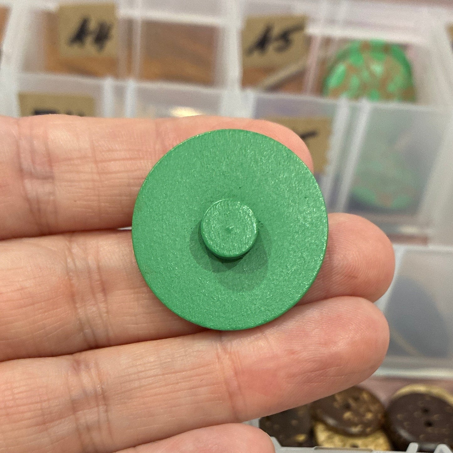 Hand holding a green button with a collection of buttons in a clear organizer.
