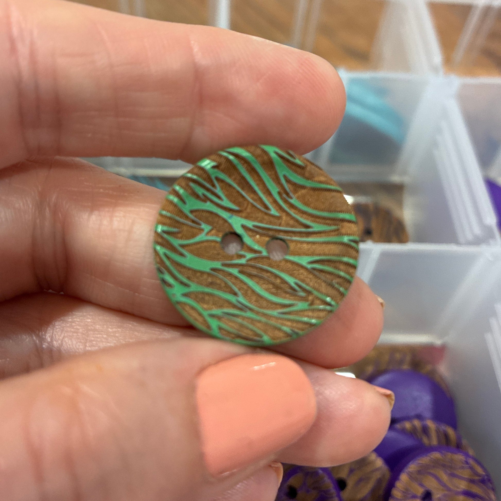 Hand holding a button with a green and brown pattern in front of a container with more buttons.