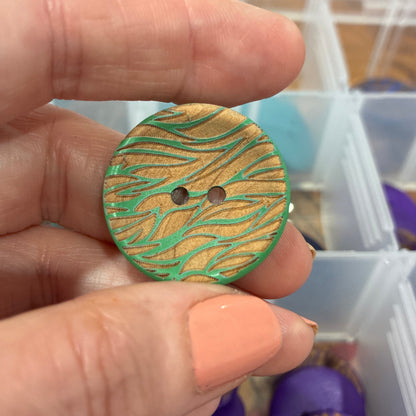 Hand holding a patterned button with a container of buttons in the background