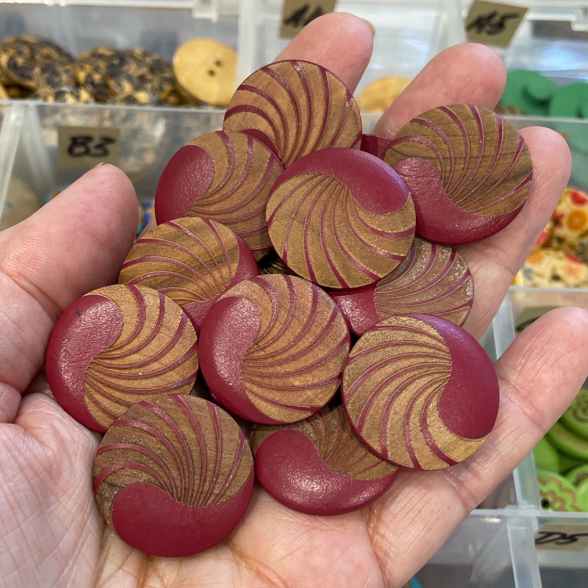 Hand holding a collection of wooden buttons with a blurred background of button display cases.