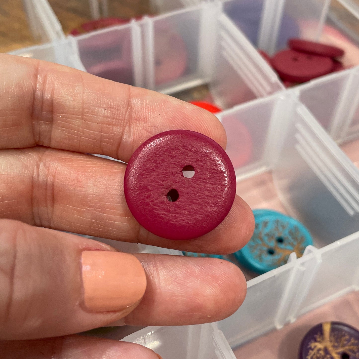 Hand holding a red button with a container of buttons in the background