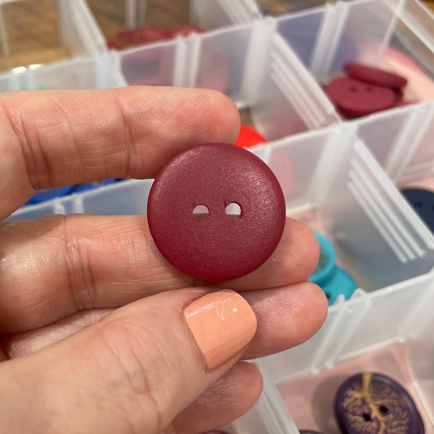 Hand holding a red button with a clear container of buttons in the background