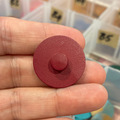 Red round button held between fingers with a background of labeled compartments.
