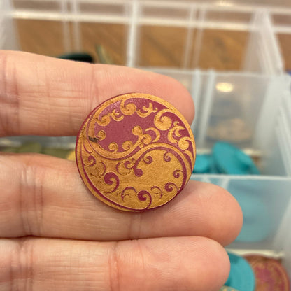 Close-up of a hand holding a decorative button with a blurred background of a storage box with buttons.
