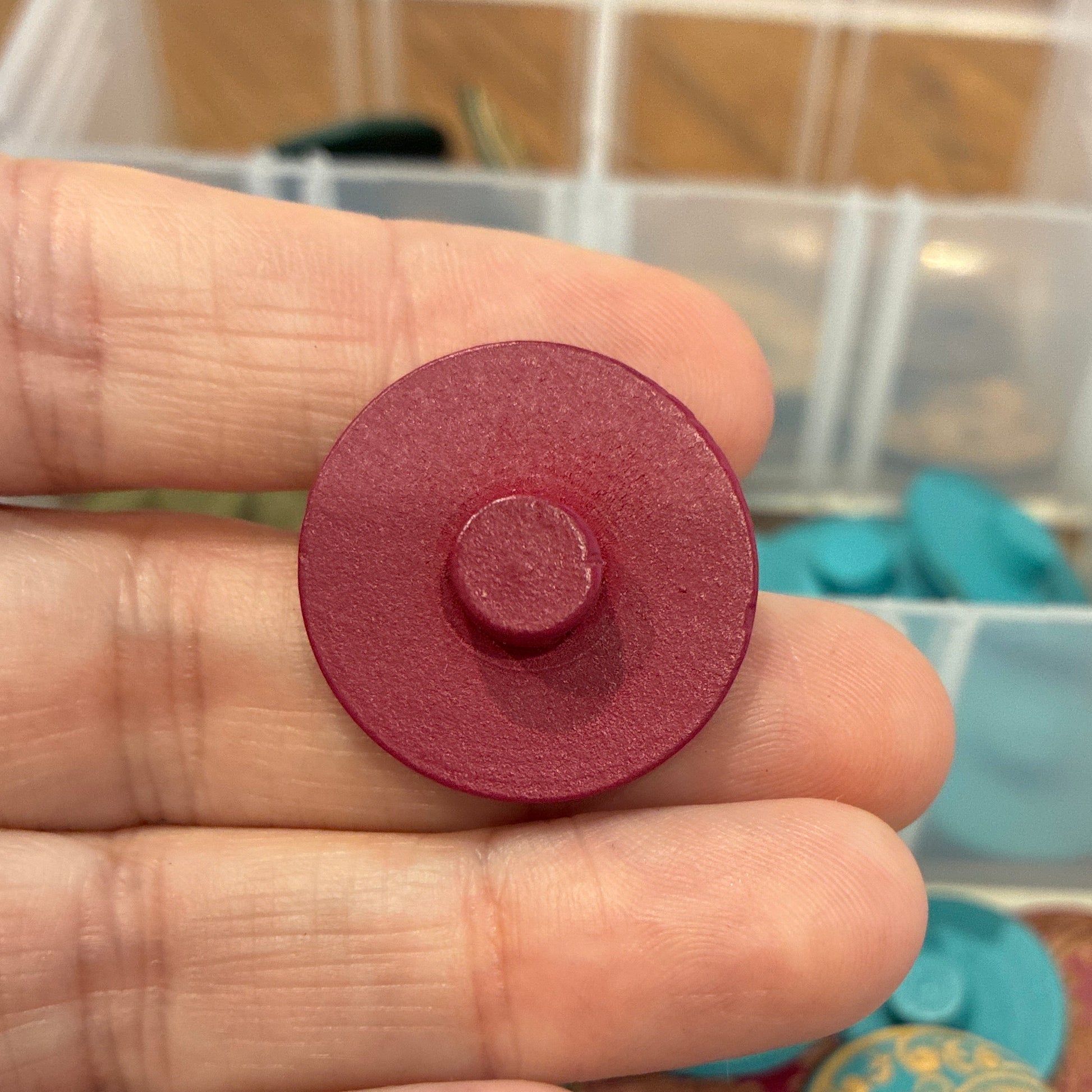 Close-up of a hand holding a red button with a container of colorful buttons in the background.