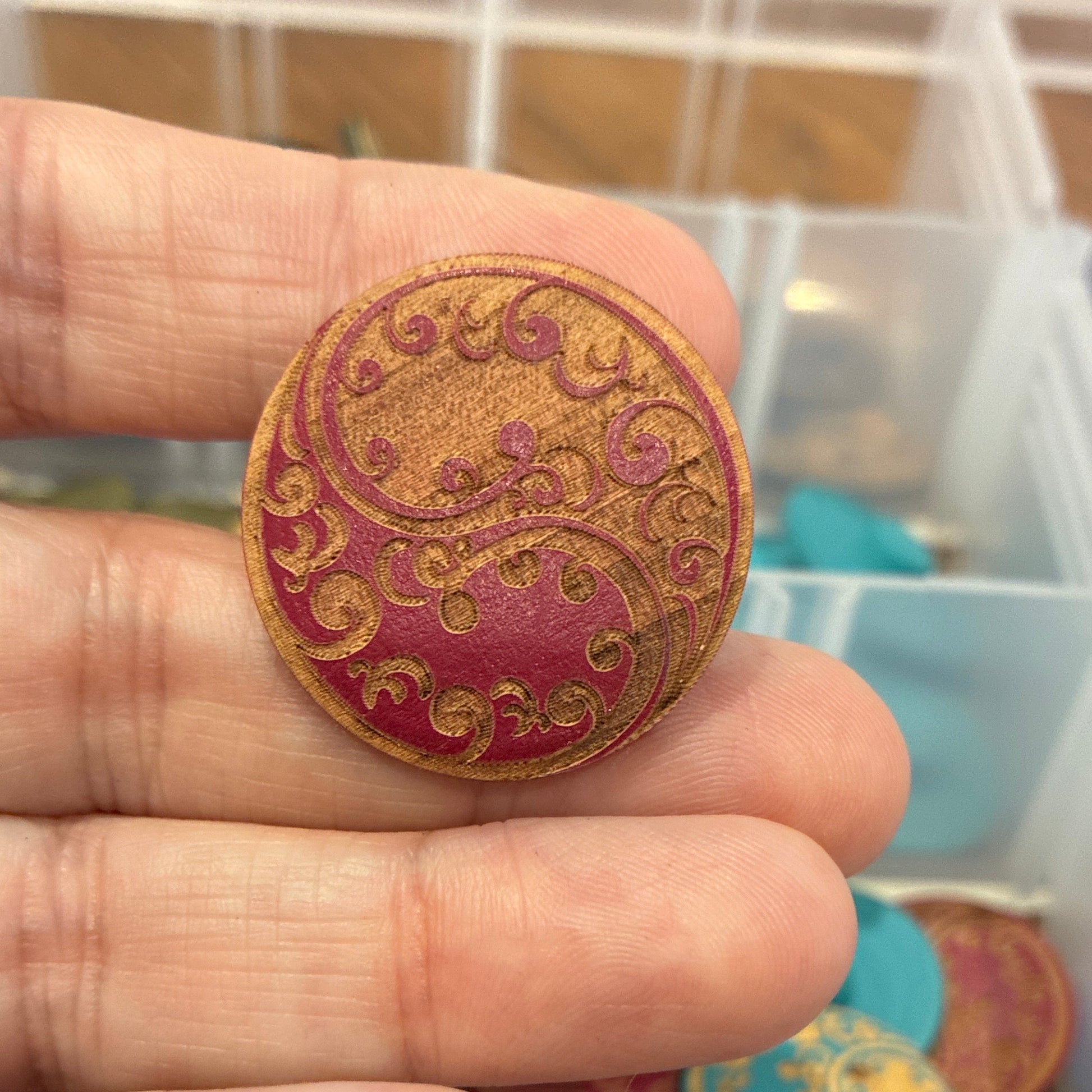 Close-up of a hand holding a decorative button with a collection of buttons in the background.