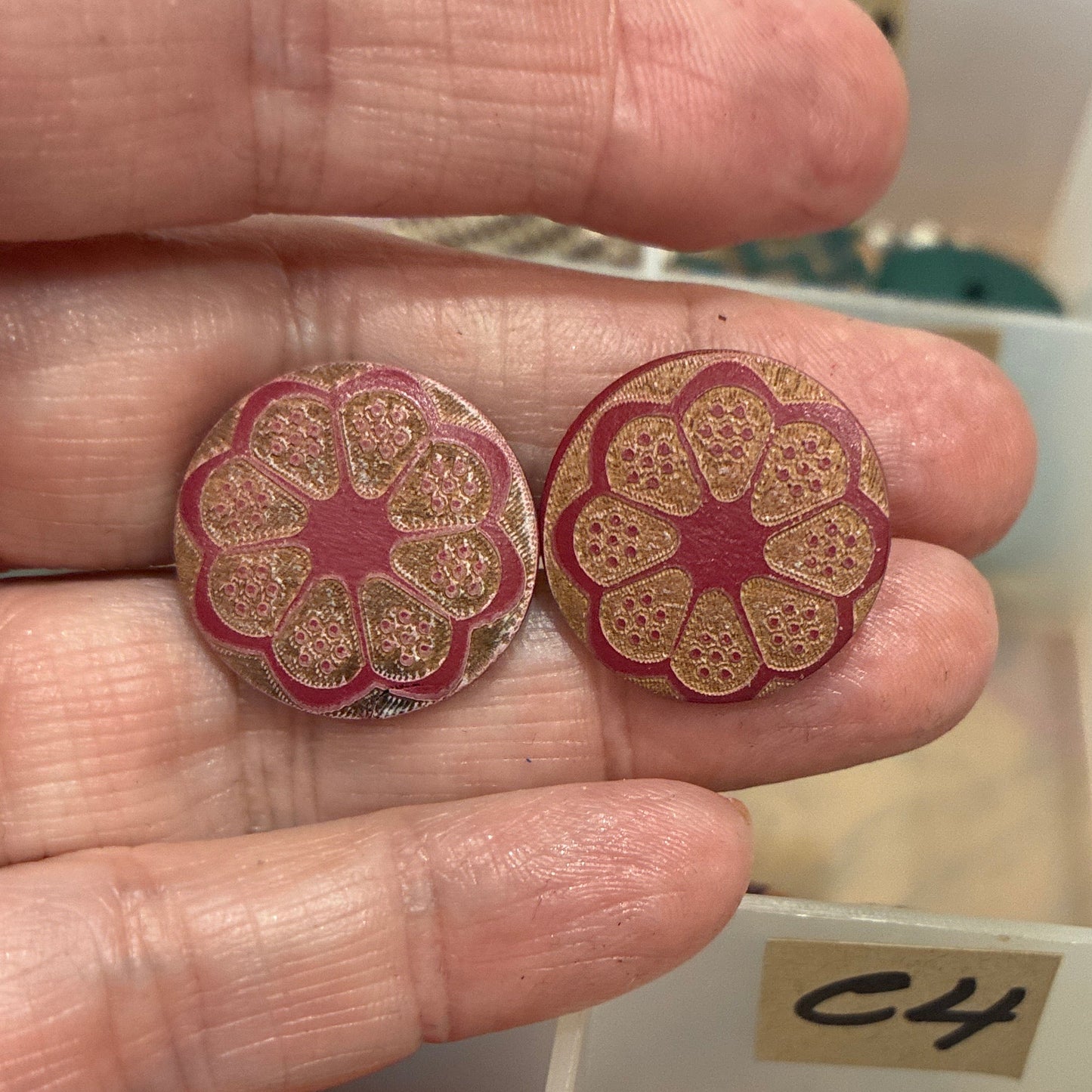 Decorative buttons held in a hand with a display of various buttons in the background.