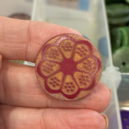 Hand holding a floral-patterned button with a container of buttons in the background