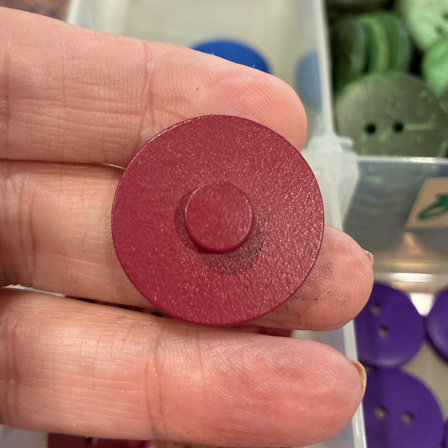 Red button held in a hand with a container of buttons in the background