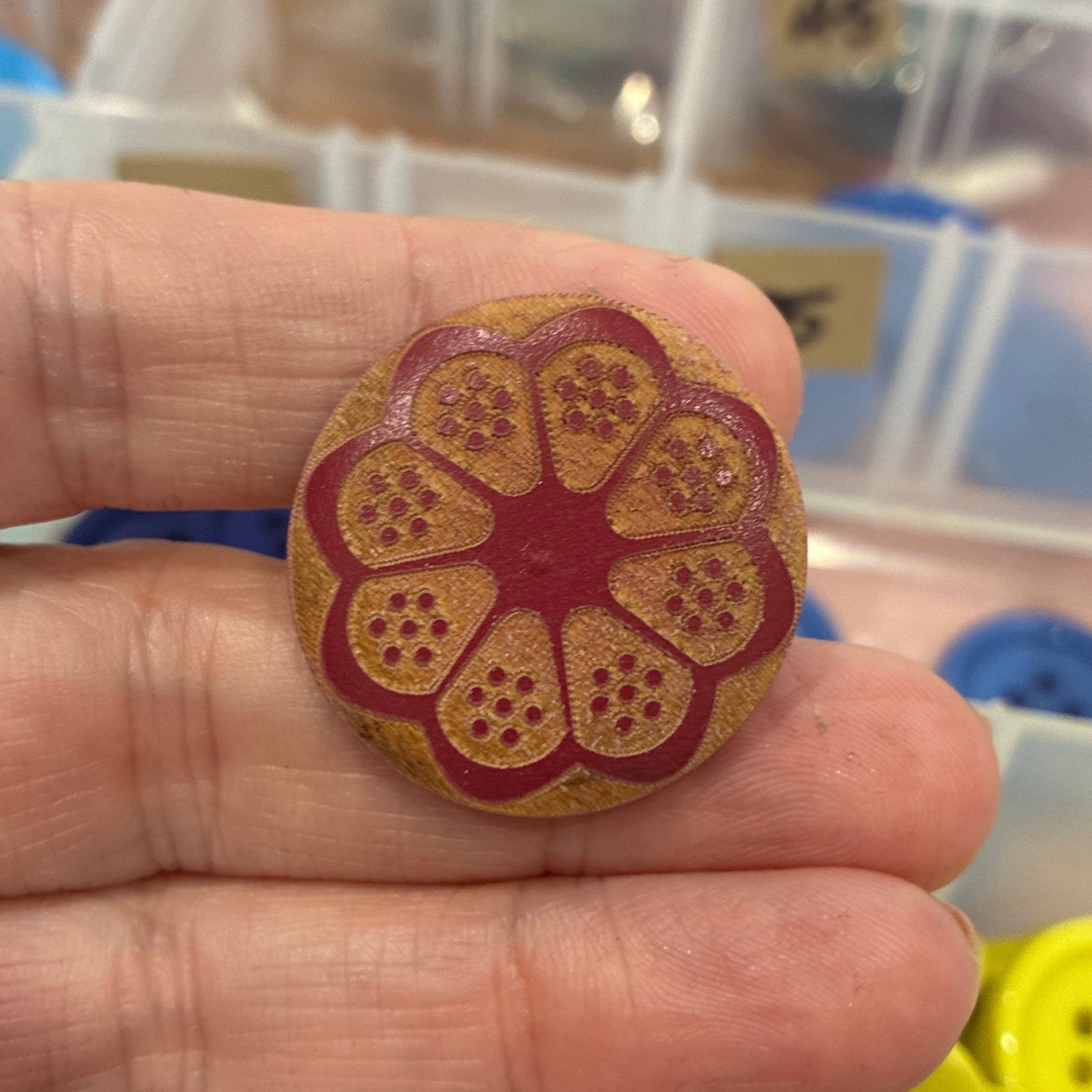 Hand holding a decorative button with a floral design, surrounded by various buttons in the background.