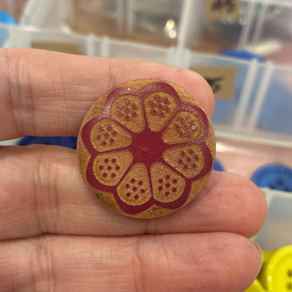 Hand holding a decorative button with a floral design, surrounded by various buttons in the background.