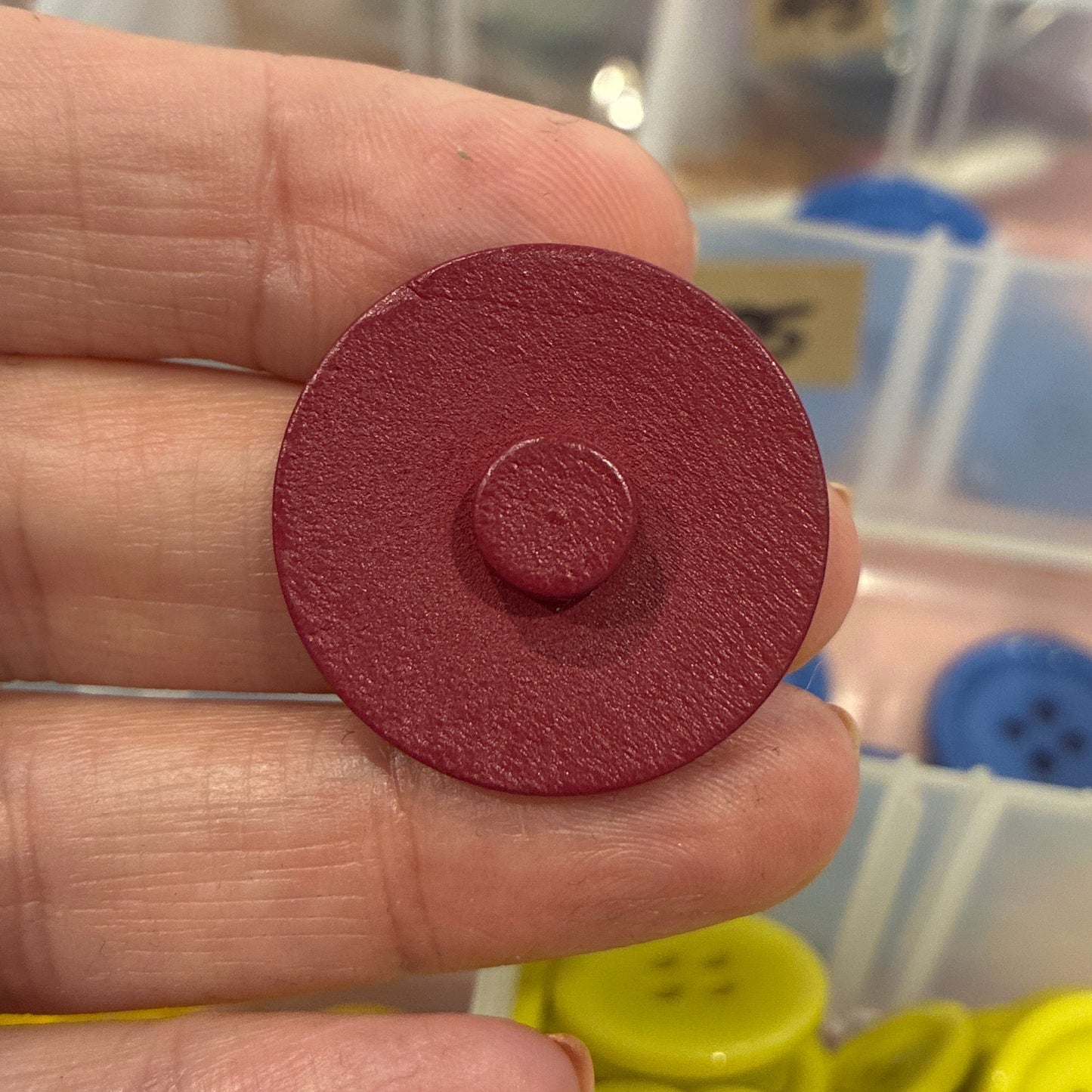 Hand holding a red button with a background of colorful buttons in containers.