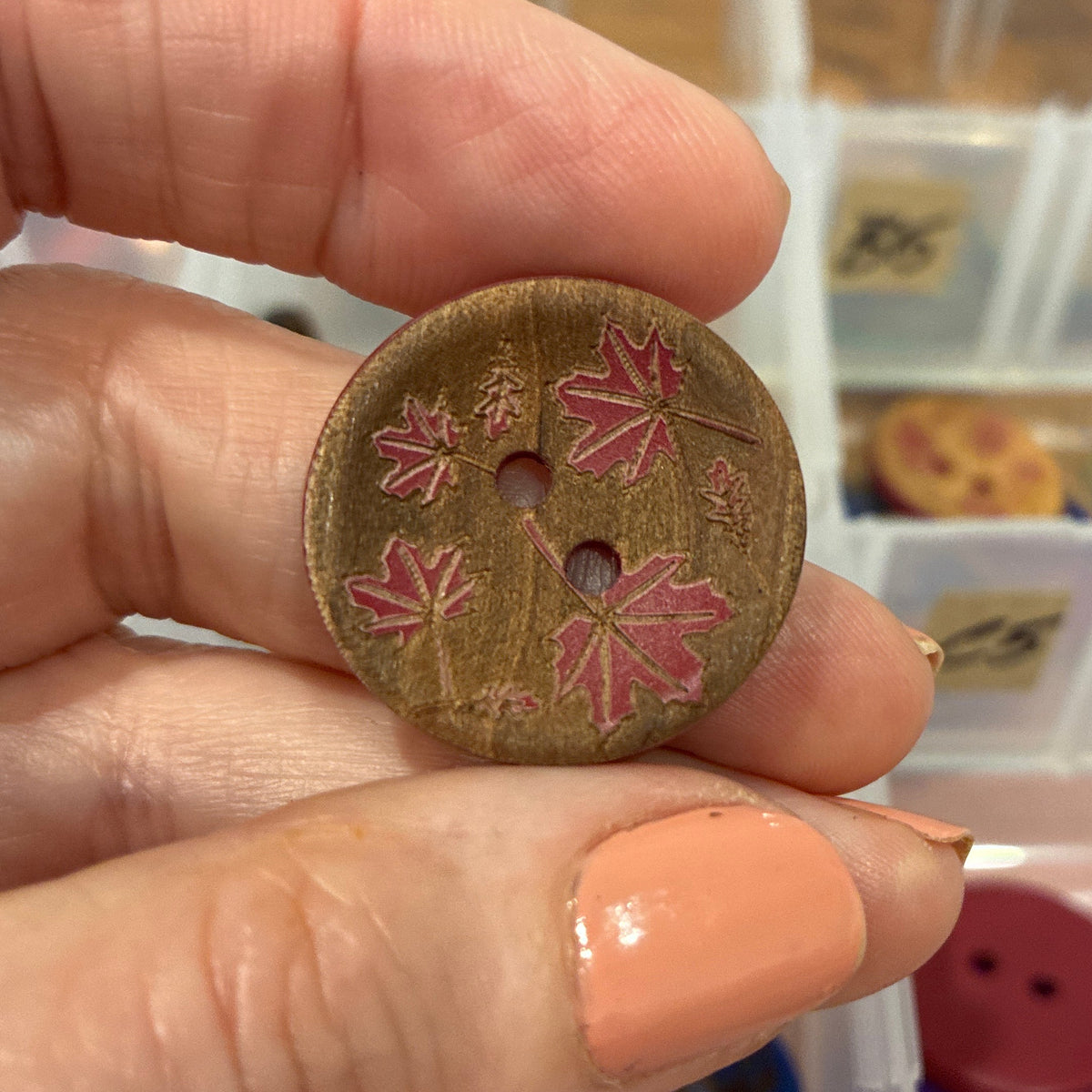 Hand holding a decorative button with floral design in front of a container of buttons.