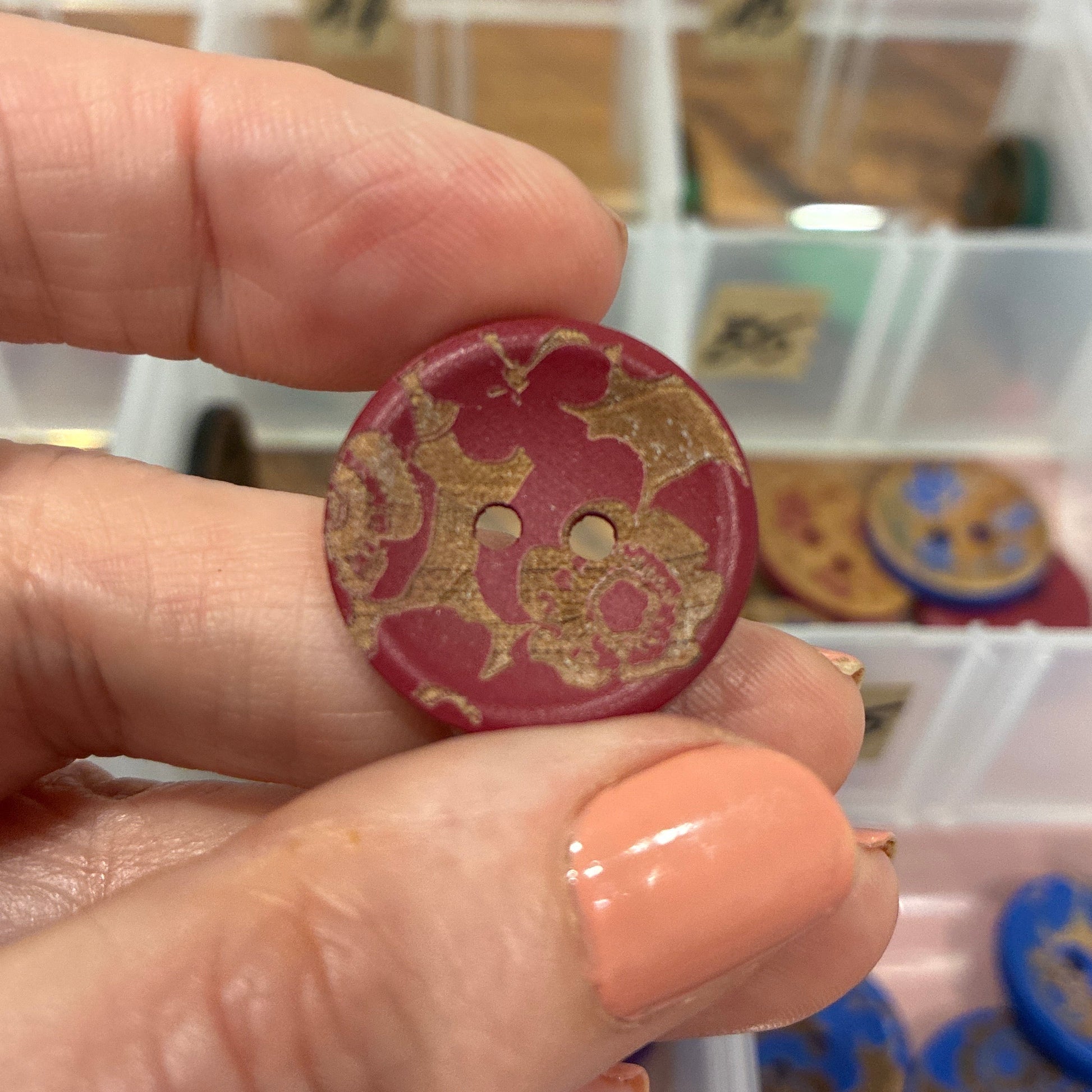 Hand holding a decorative button with a blurred background of a button collection container.