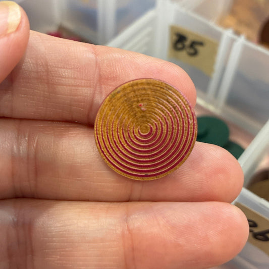 Hand holding a gold spiral button with a collection of similar buttons in the background.