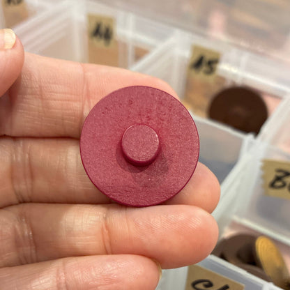 Hand holding a red circular button with a collection of similar objects in a box in the background
