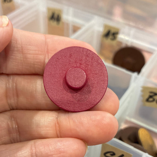 Hand holding a red circular button with a collection of similar objects in a box in the background