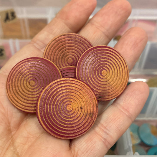 Hand holding circular wooden buttons with a blurred background of a storage box with craft supplies.