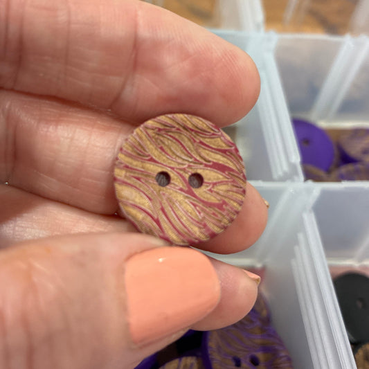 Hand holding a wooden button with a button organizer in the background