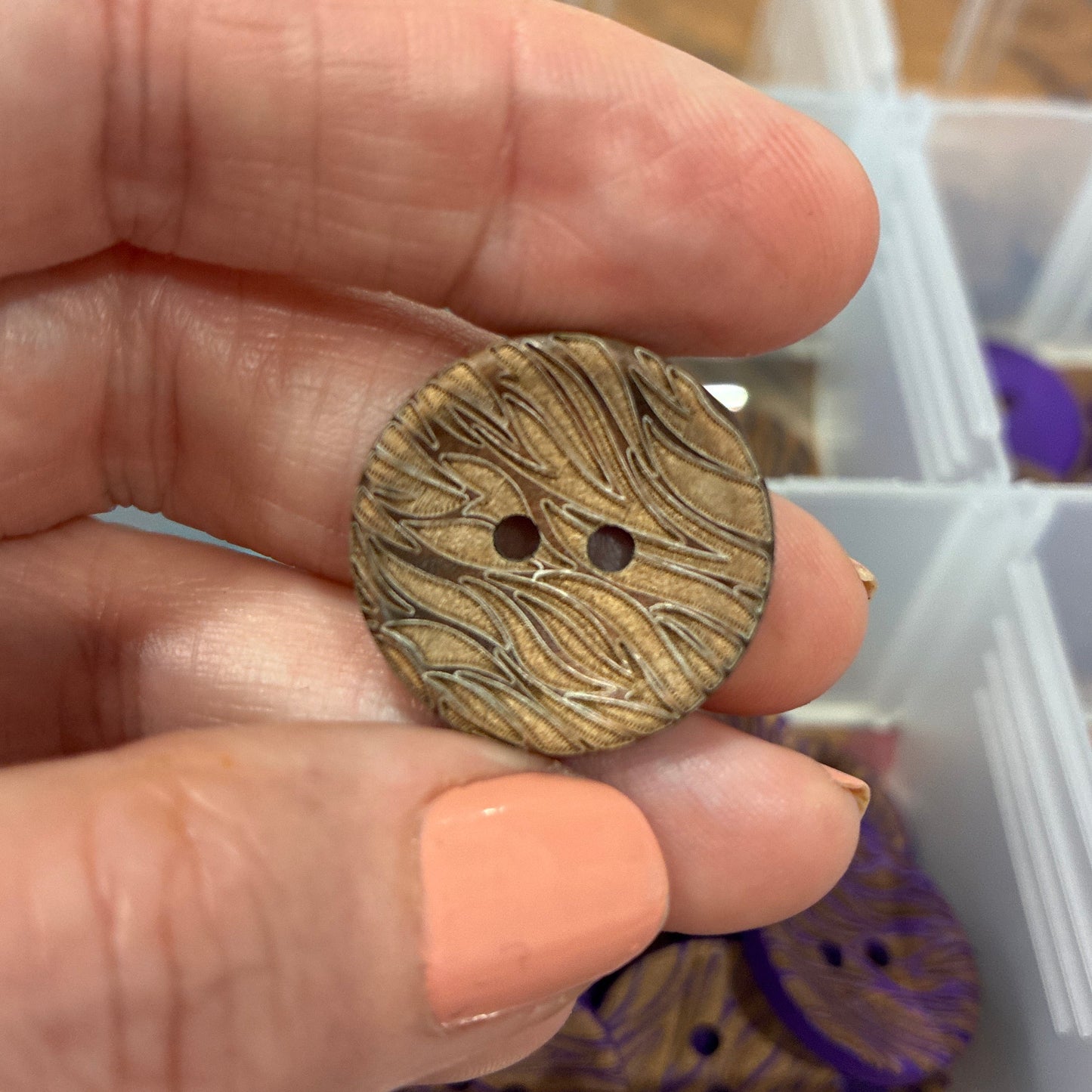 Hand holding a wooden button with a blurred background of storage containers.