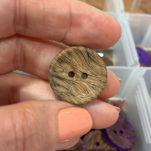 Hand holding a wooden button with a blurred background of storage containers.