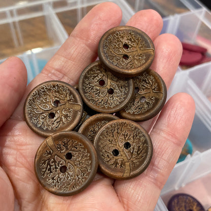Hand holding a collection of ornate bronze buttons with a blurred background