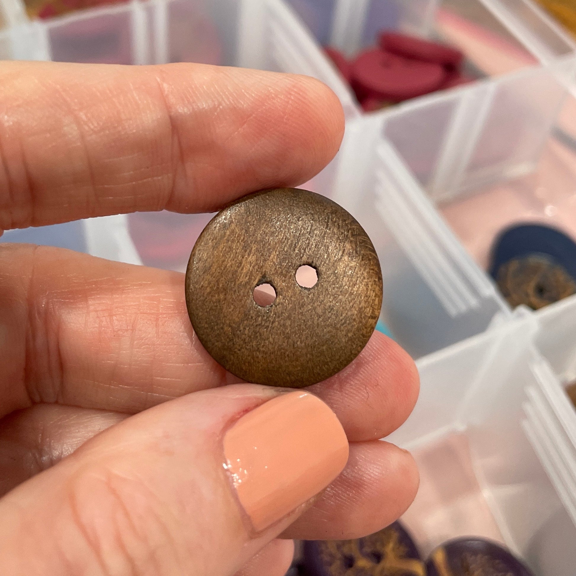 Hand holding a bronze button with a container of buttons in the background