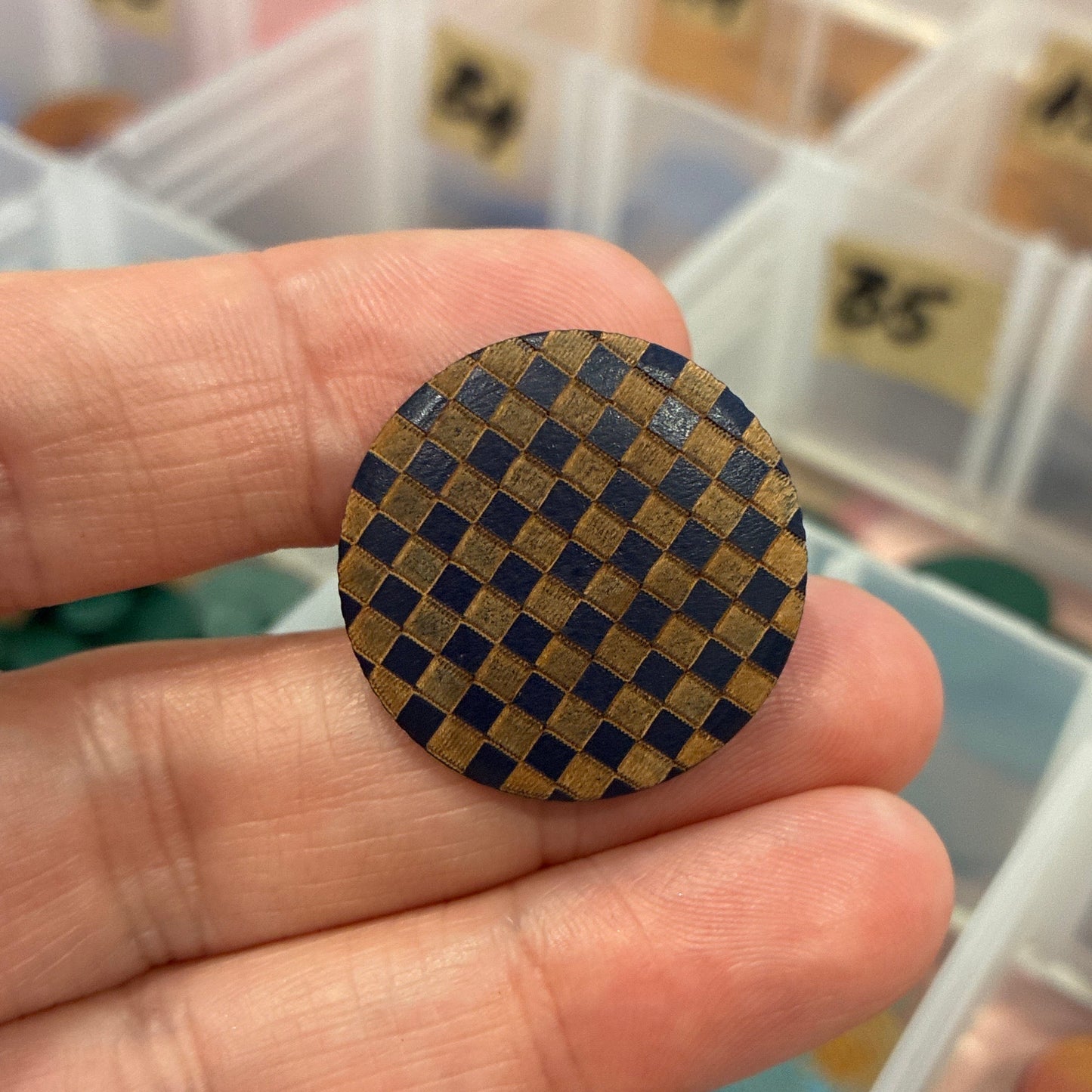 Hand holding a checkered button with a container of buttons in the background