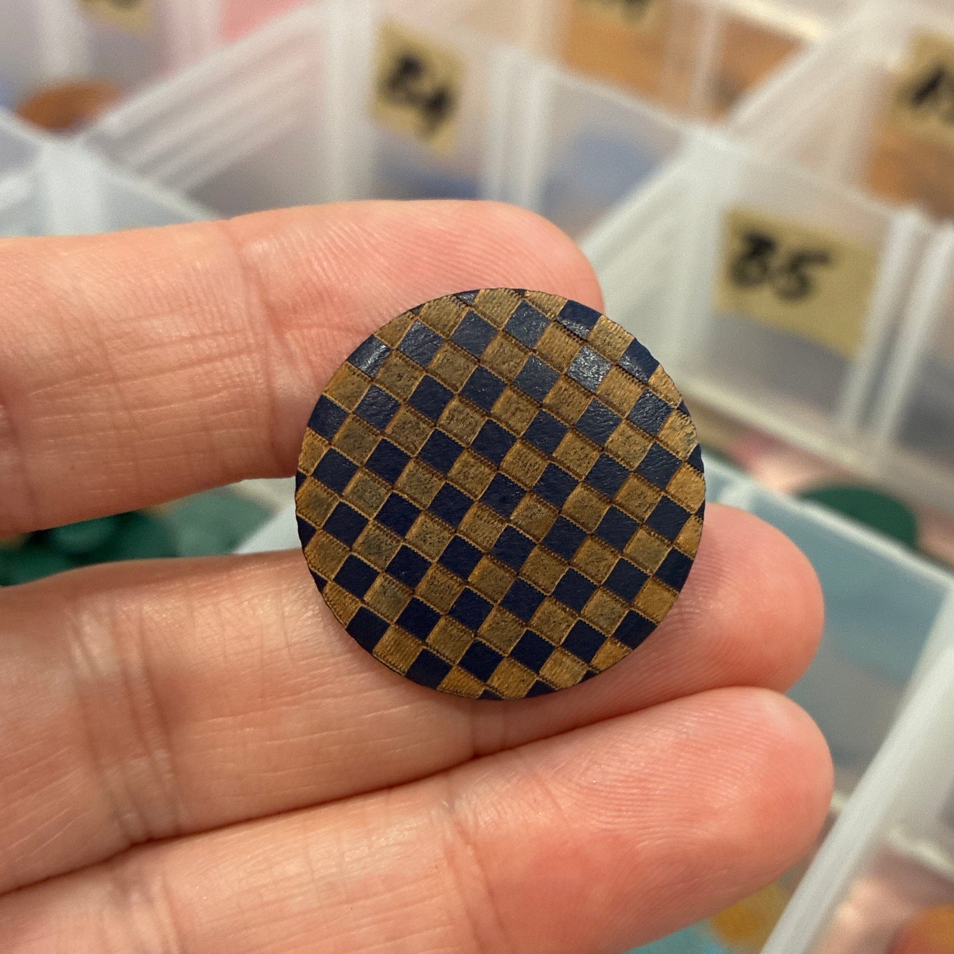 Hand holding a checkered button with a container of buttons in the background