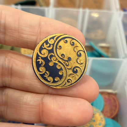 Gold and black circular decorative item held between fingers with a colorful background