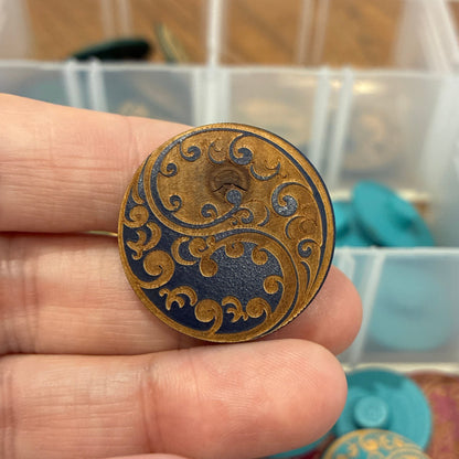 Hand holding a decorative button with a blurred background of a storage box with buttons.