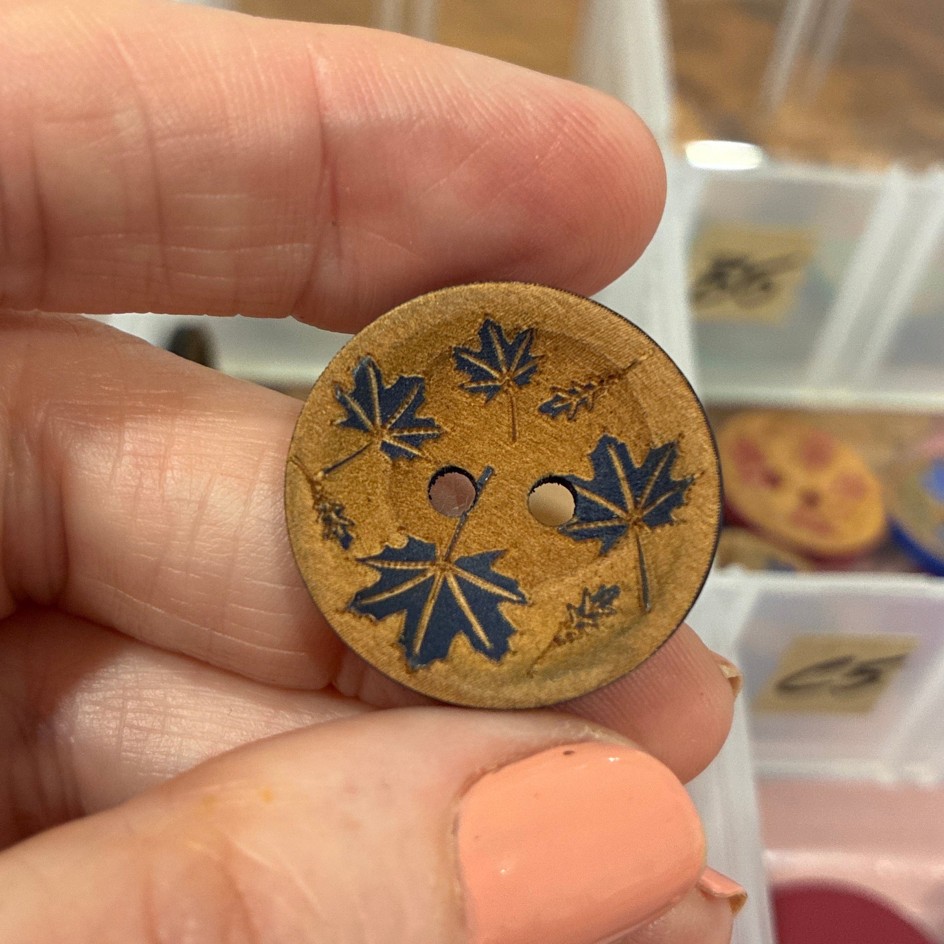Hand holding a decorative button with floral patterns in front of a container of buttons.
