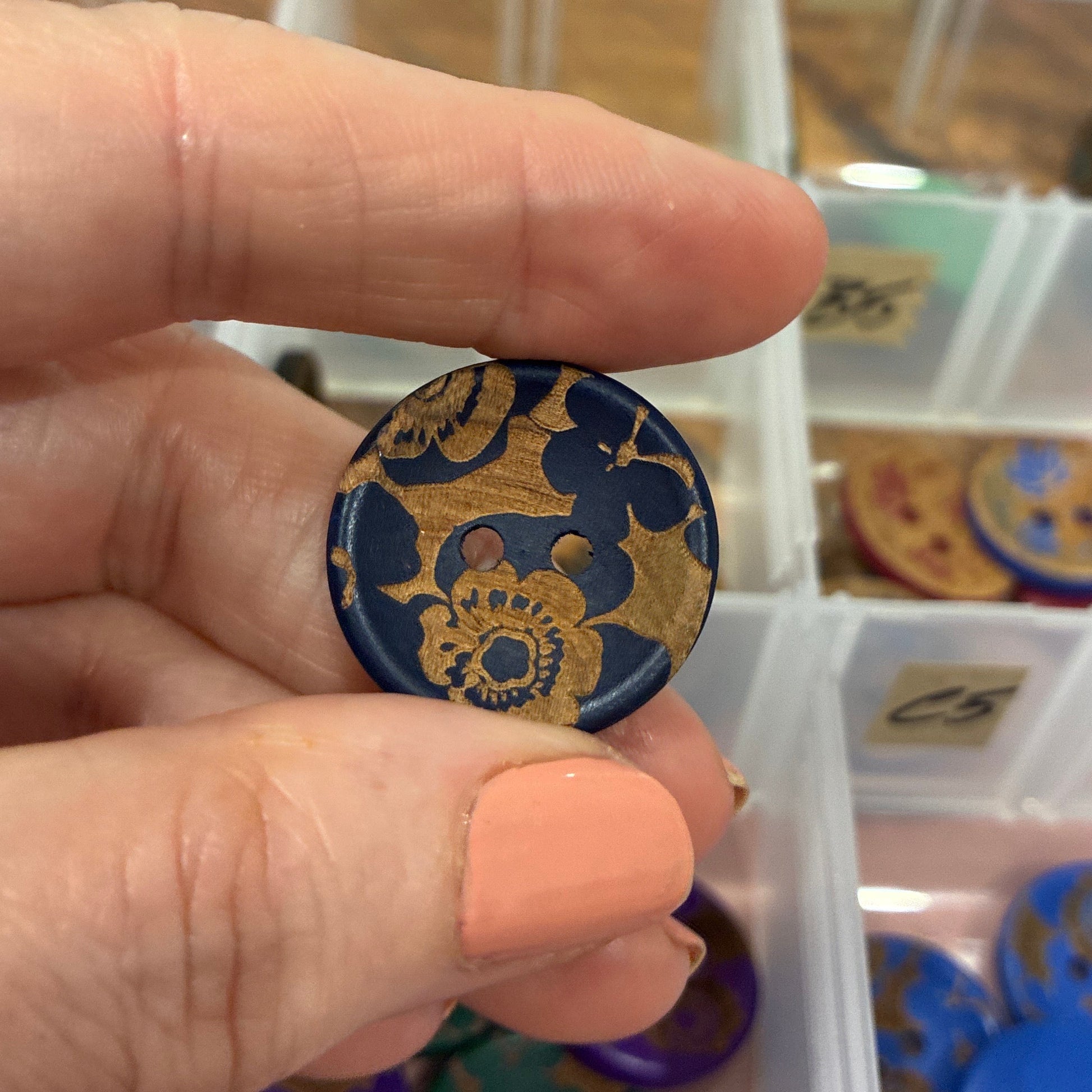 Hand holding a decorative button with a blurred background of button collection