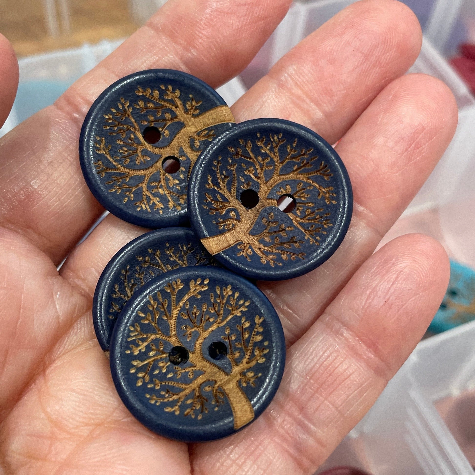 Hand holding decorative buttons with intricate designs, with a container of buttons in the background.