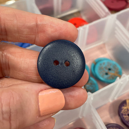 Hand holding a blue button with a container of buttons in the background