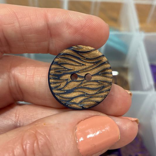 Hand holding a wooden button with a pattern, with a background of a storage box containing various items.