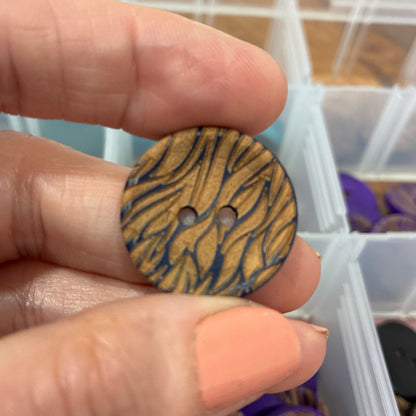 Hand holding a wooden button with zebra pattern in front of a clear container with more buttons.