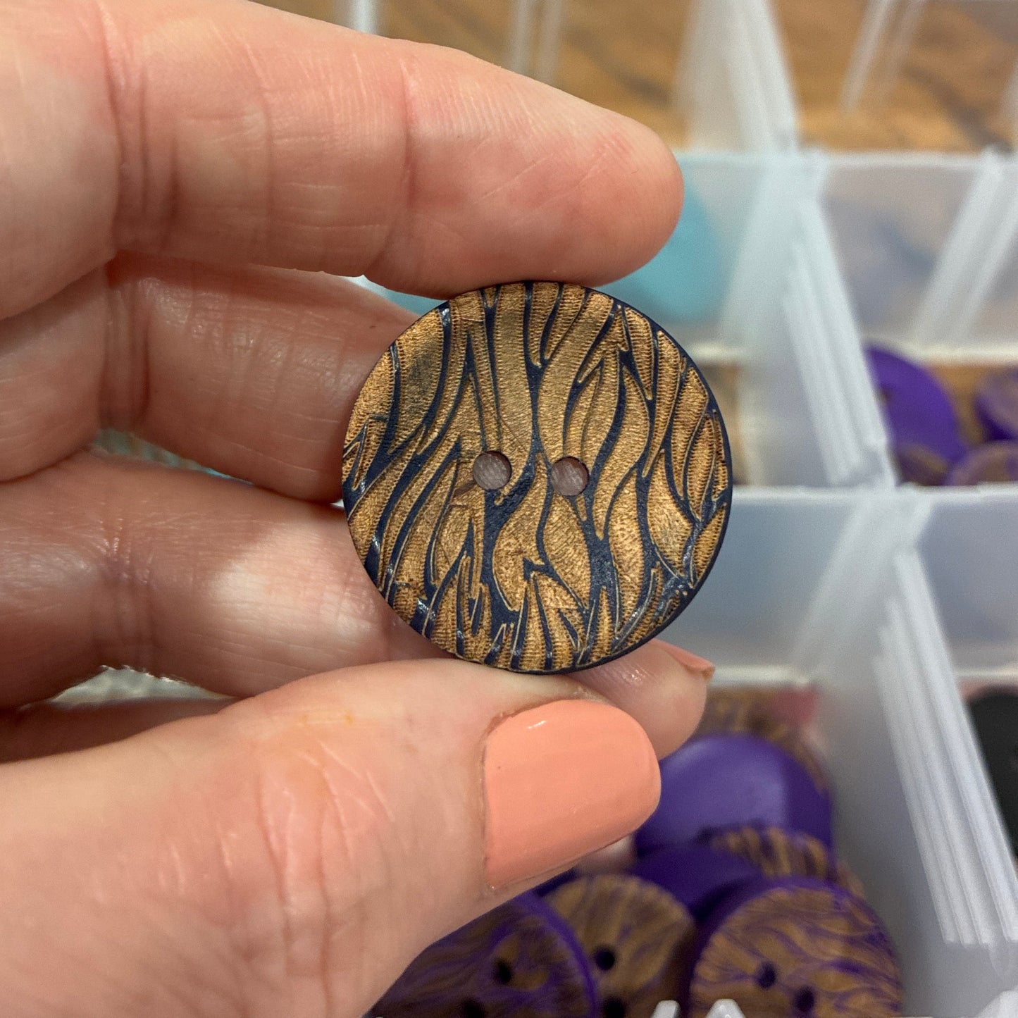 Hand holding a wooden button with zebra pattern over a container of similar buttons.
