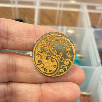 Gold decorative button held between fingers with a container of colorful items in the background