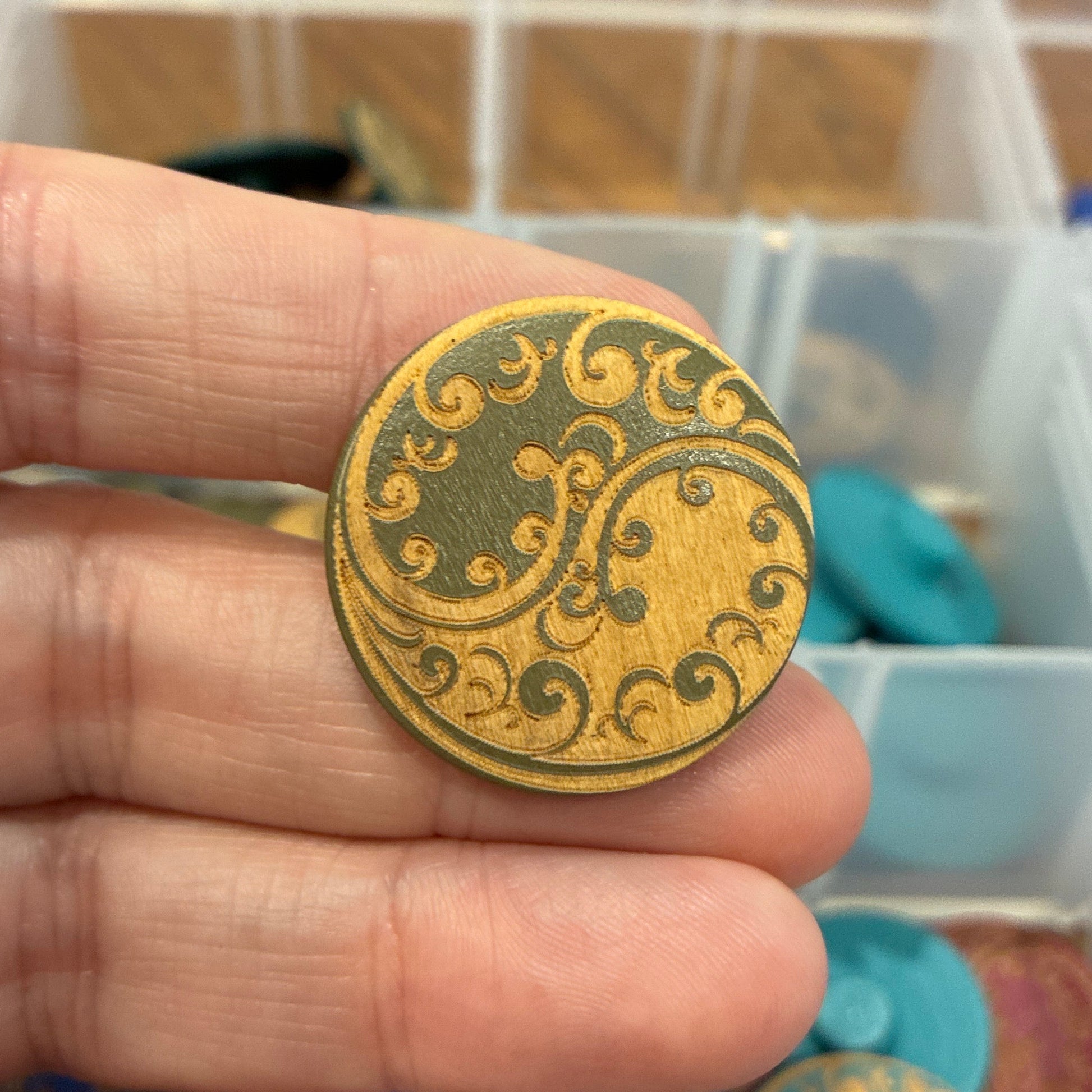 Gold decorative button held between fingers with a container of similar buttons in the background