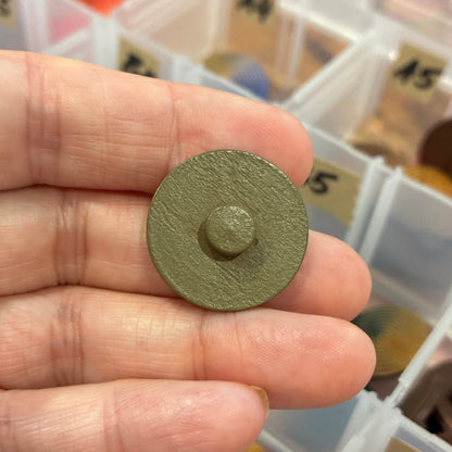 Hand holding a round metallic button with a colorful organizer in the background