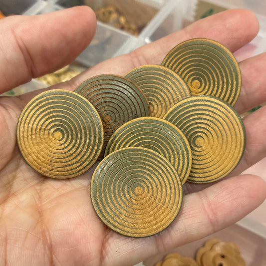 Hand holding gold spiral buttons with a background of button collection in a box.