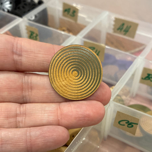 Hand holding a gold spiral button with a container of various buttons in the background