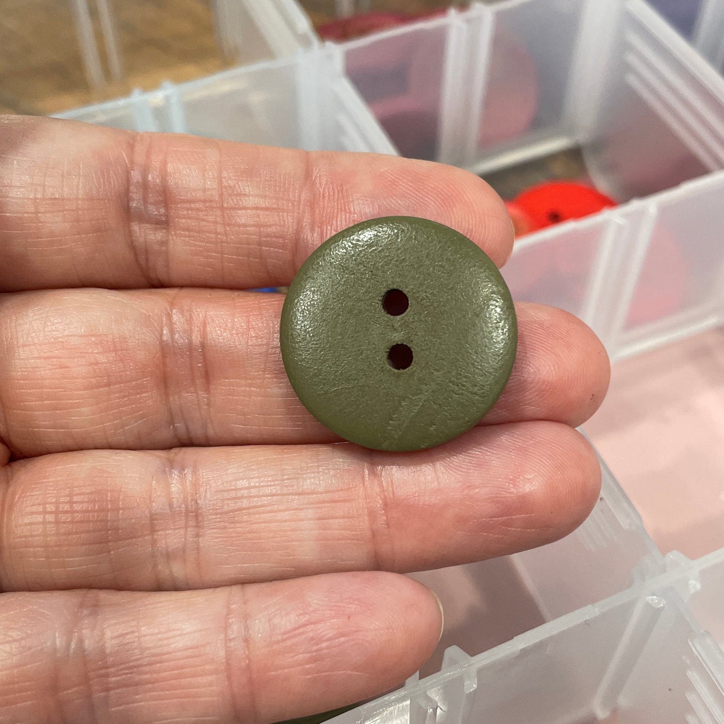 Hand holding a green button with a container of buttons in the background