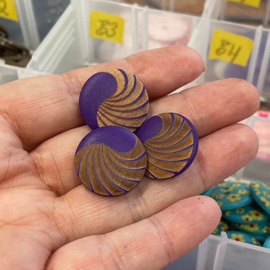 Hand holding two decorative buttons with a container of assorted buttons in the background.