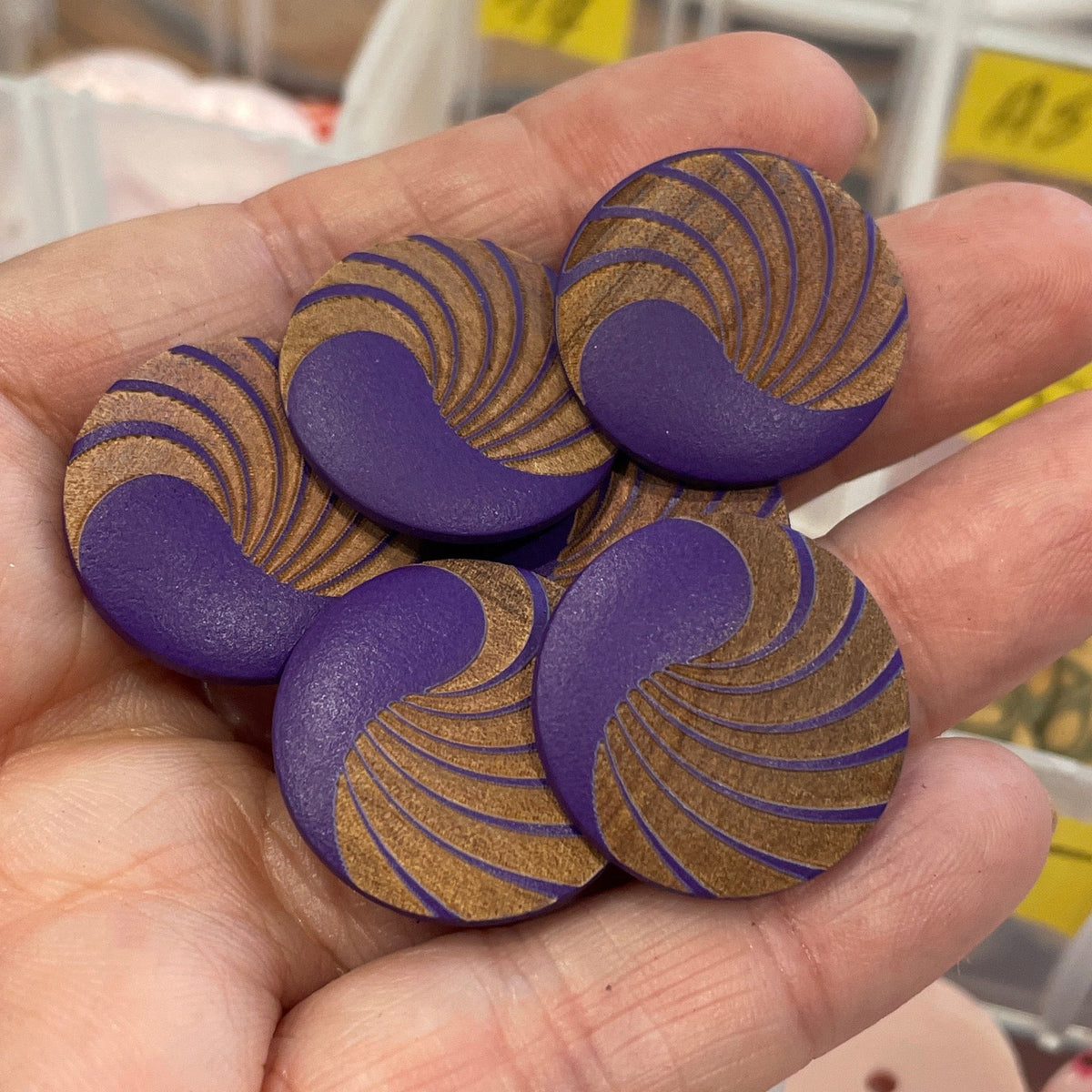 Hand holding decorative buttons with a background of button storage containers.