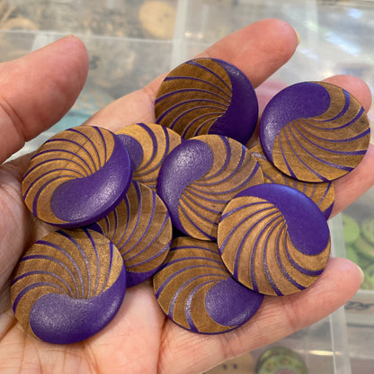 Hand holding purple and gold patterned buttons with a blurred background